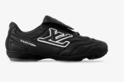 Side view of a black Louis Vuitton Footprint soccer shoe with white LV logo and Vuitton text.