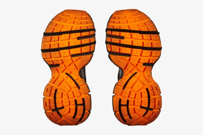 Bottom view of Balenciaga 3XL sneakers showing bright orange textured rubber outsoles with black details. - SKU 734734W3XL31178