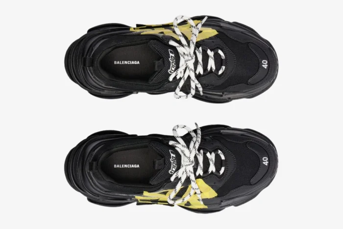 Top-down view of black Balenciaga Triple S Tapa Type sneakers featuring yellow tape accents and white laces. - SKU 536737WTRST1070