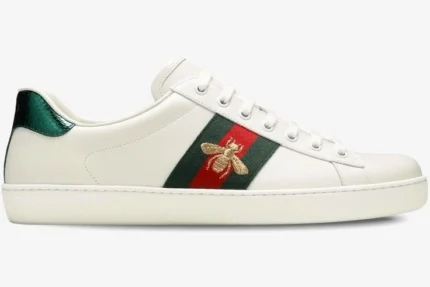 Side view of white Gucci Ace leather sneakers featuring a gold embroidered bee on a green and red web stripe. - SKU 42944602JP09064