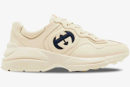 Side view of a Gucci Rhyton sneaker in ivory leather featuring a navy blue interlocking G logo. - SKU 757857UPG709567