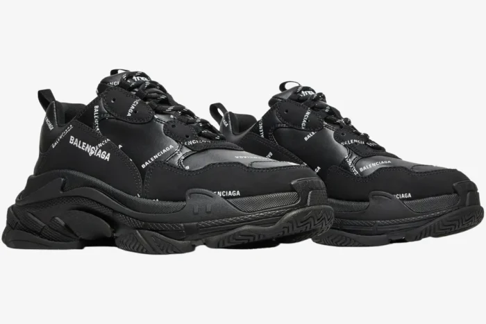 Black Balenciaga Triple S sneakers with white allover logos, shown in a three-quarter side view.