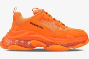 Side profile of a bright orange Balenciaga Triple S sneaker with a chunky clear sole.