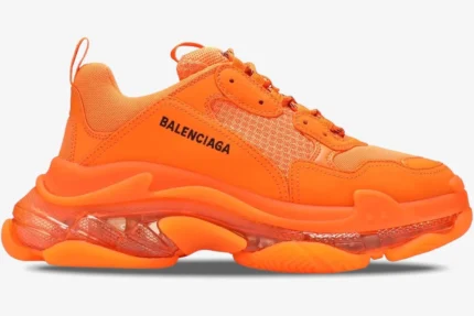 Side profile of a bright orange Balenciaga Triple S sneaker with a chunky clear sole.