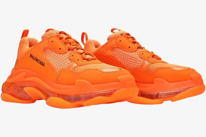 Balenciaga Triple S sneakers in vibrant orange with a clear sole, shown from a three-quarter side angle.