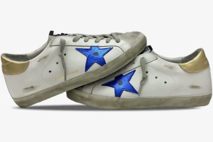 Side view of two Golden Goose Super-Star sneakers in distressed white leather with navy stars and gold heels. - SKU GMF00101.F000312.10272