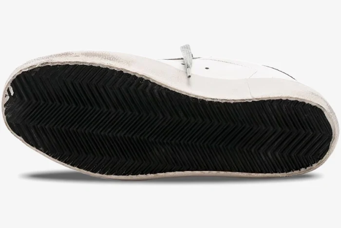 Bottom view of a Golden Goose Super-Star sneaker showing the black herringbone rubber outsole and distressed white midsole. - SKU