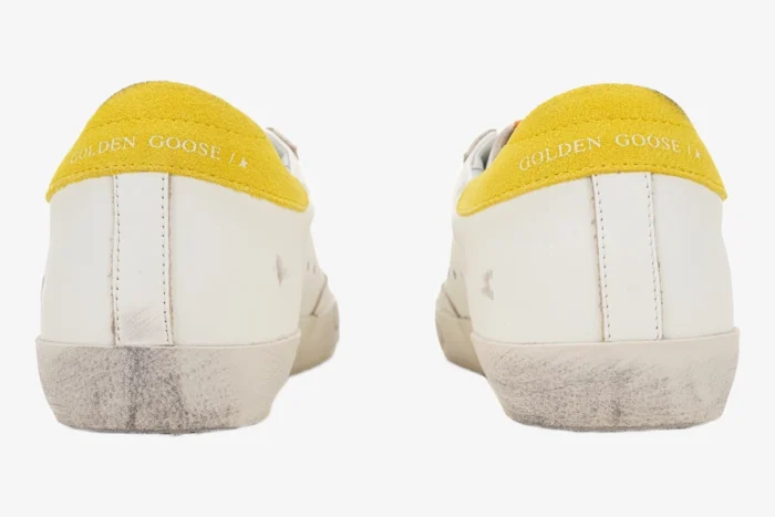 Rear view of Golden Goose Super-star sneakers in white with yellow suede heel tabs and distressed soles. - SKU GWF00101.F002559.10928
