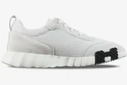 Side profile of Hermes Bouncing Sneakers in white mesh and grey suede with a black rubber sole detail. - SKU H202934ZH